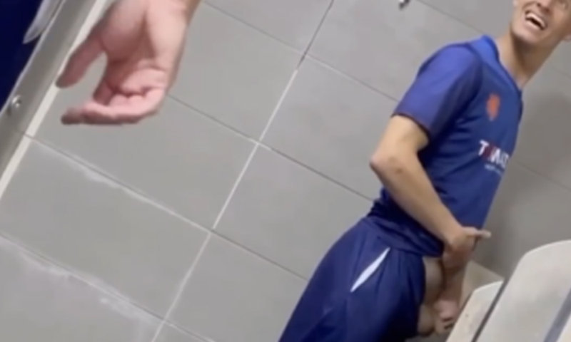 guy in football uniform peeing at urinals